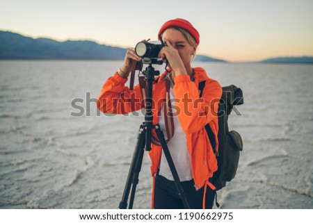 Skilled female travel photographer using tripod for shooting video of scenic landscape in desert, young woman taking photos via professional equipment on exploring Badwater basin in National Park