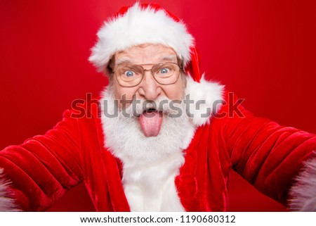 Close up aged face playful funky stylish grandfather Santa fooling around take selfie on smartphone camera show tongue out isolated on bright red background