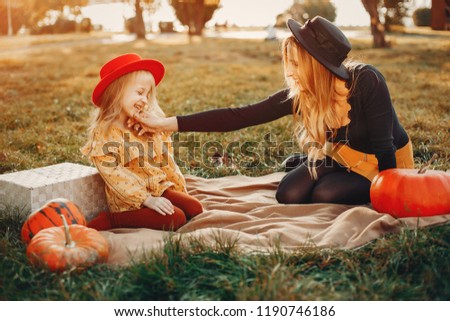 Stylish mother with cute little daughter in a park. Family with pumpkin. Little girl in a red hat