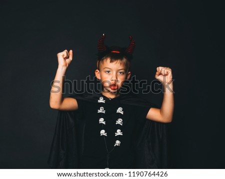 little boy with red halloween horns and black cape in front of black background