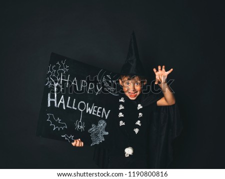 young boy dressed as a magician is holding happy halloween chalkboard in front of black background