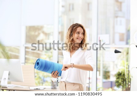 Young beautiful businesswoman holding yoga mat in office. Gym after work