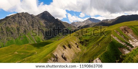 Panoramic landscape of great caucasian mountain range. Amazing nature and ecology concept of big mountains with green fields, high rocks and blue cloudy sky in sunny summer day. Russia, Elbrus region.
