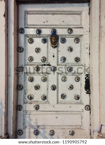 Distressed old white door with men face in the middle as the knocker and little distressed metal knobs around the whole door.