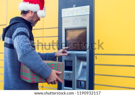 man client with santa hat using automated self service post terminal machine or locker to deposit the parcel for storage