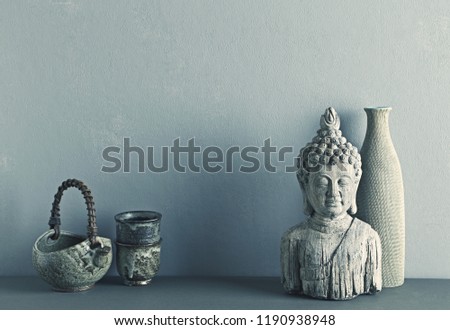 An arrangement of hand crafted Asian ceramics and a stone Buddha statue. Copy space. Gray background