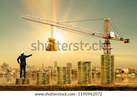 Man engineers is working on stack gold coin with grow value and tower crane and hoist brake with money bag on photo blur cityscape background, Loan and budget  for construction real estate concept.