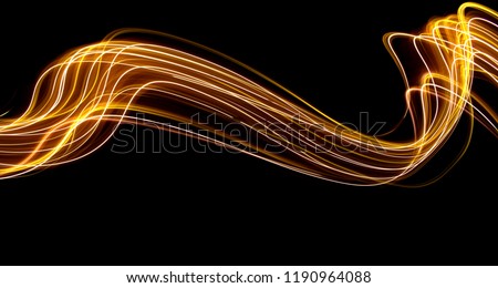 Long exposure light painting photography, curvy lines of vibrant neon metallic yellow gold against a black background Royalty-Free Stock Photo #1190964088