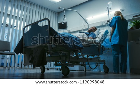 Low Level Shot in the Hospital, Very Sick Man Lying on the Bed, Nurse Checks His Vital Signs and Drop Counter.