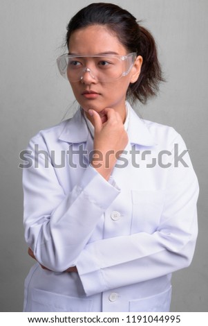 Young beautiful Asian woman doctor wearing protective glasses against dirty white wall background
