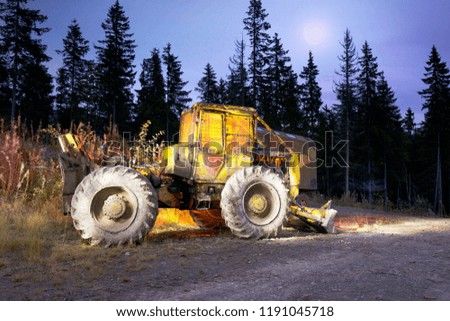 An ancient tractor at the top of the mountain for transportation of coniferous forest is illuminated by a photographer of various lights in the moonlit night in the Carpathians as an art object