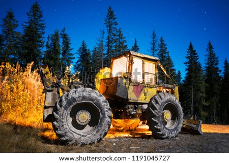 An ancient tractor at the top of the mountain for transportation of coniferous forest is illuminated by a photographer of various lights in the moonlit night in the Carpathians as an art object