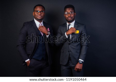 two young successful businessman partners men in a stylish black classic suit and in cool glasses holding a yellow plastic credit card in the studio on a dark background. shopping concept