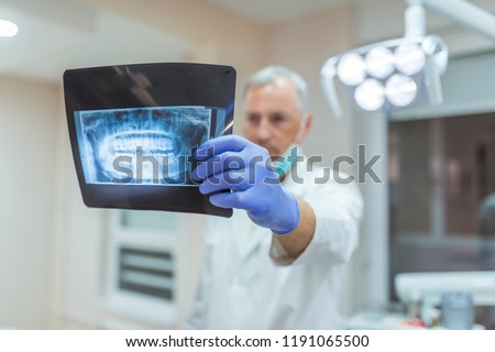 Picture of male doctor or dentist looking at x-ray. Dentist Doctor Looking at X-ray at the Hospital.  Concentrated male dentist looking at x-ray. X-ray of a human jaw in the hands of the dentist.
