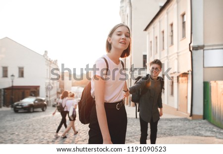 Attractive girl holds a young man by the hand and goes with him along the street of the old town on the background of the sunset. Happy man follows a girl on the background of the sunset. Follow me.