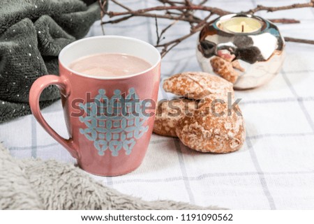 A cup of cocoa in an interesting cozy atmosphere is surrounded by branches with snow and a candle