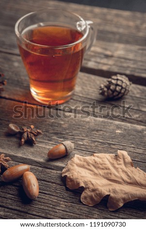 Autumn background concept on a wooden table with a glass cup of tea, oak leaf, Pine cones and acorns