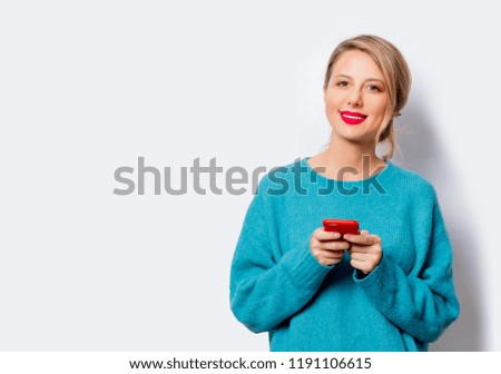 Portrait of a beautiful white smiling woman in blue sweater with mobile phone on white background, isolated.