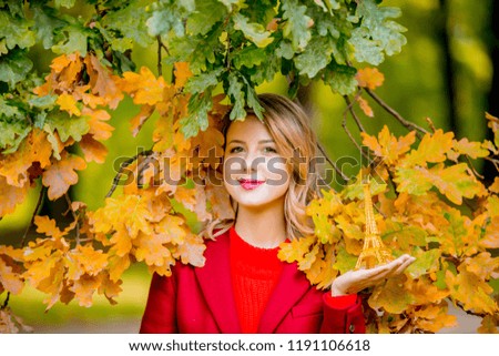 Portrait of a young cozy woman with Eiffel tower toy near oak tree in autumn season park.