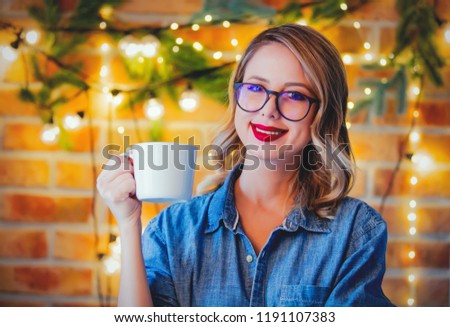 Portrait of a young cozy woman with cup of coffee and Christmas lights and pine branch
