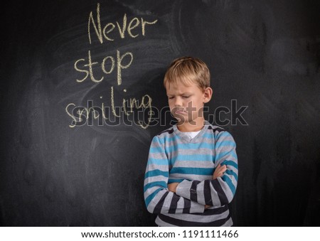 gloomy European boy at the black Board with the inscription " never stop smiling"