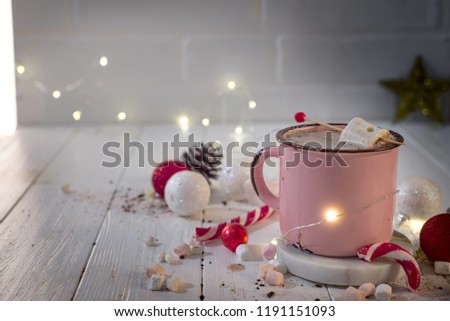 Enamel cup of hot cocoa with mini marshmallows and candy canes with beautiful Christmas lights of bokeh. Christmas concept