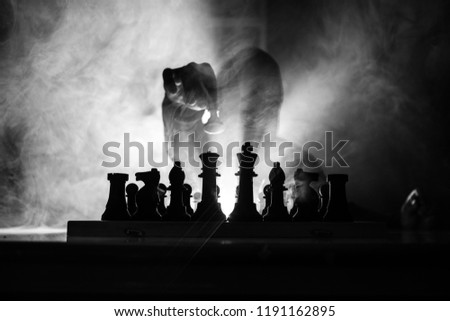 Man playing chess. Scary blurred silhouette of a person at the chessboard with chess figures. Dark toned foggy background. Selective focus. Horror concept