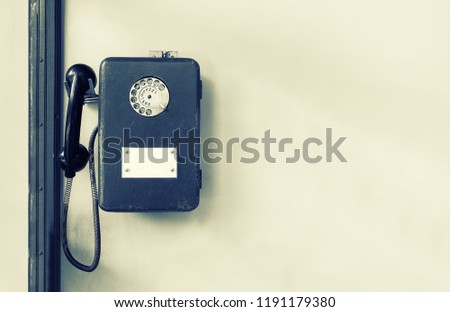 Old public payphone on the wall. Metal phone. Disk telephone. Black and white toned photo. Royalty-Free Stock Photo #1191179380