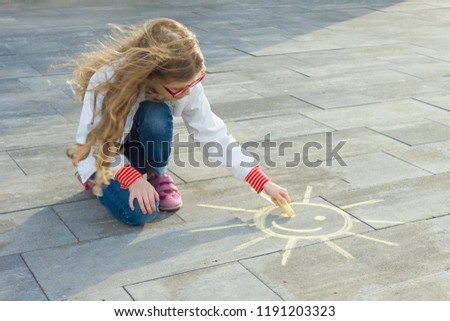 Child girl draws the symbol of the sun with colored crayons on the asphalt.