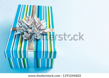 One gift box wrapped in blue striped paper and tied with a silver bow on a blue background. The concept of the holiday, the top view, the place for the text, the banner for the site.