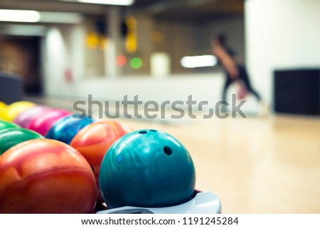 Colorful bowling balls and player throwing balls in background at bowling club.