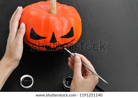 Preparation for Halloween: women's hands paint orange pumpkin with black paint. Closup. Holiday decoration concept.