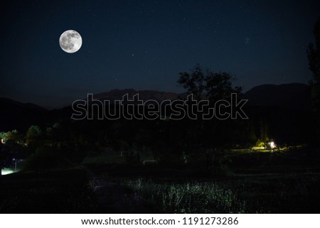Mountain Road through the forest on a full moon night. Scenic night landscape of dark blue sky with moon
