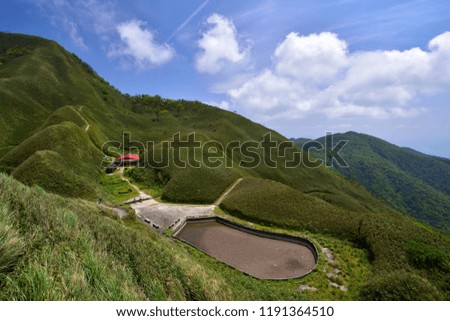 Blue sky and white clouds, hiking trails hidden in the mountains and hills, valleys of the red roof of the small house, slightly wet pond.
