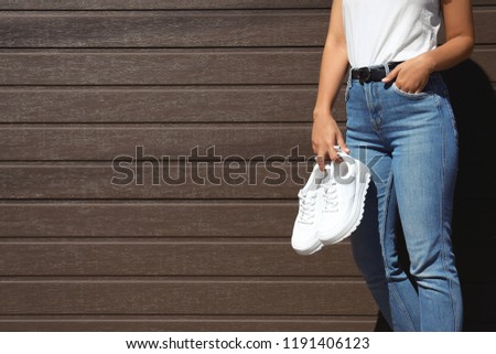 Woman holding stylish sneakers near wooden wall. Space for design