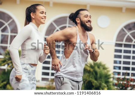 City positive runners jogging outdoor. Fit caucasian couple working out against fitness centre.