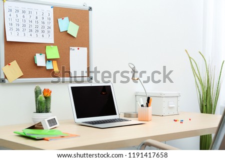 Workplace with cork board and laptop on table. Blank screen with space for text