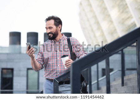 Street lifestyle. Cheerful handsome bearded man using his phone while standing outdoors