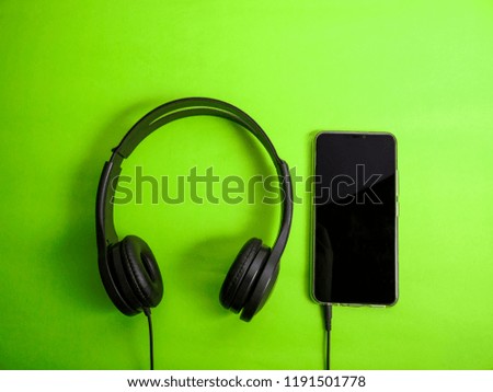 Headphone and smartphone. Earphones on green background. Listening music sound on mobile phone device concept