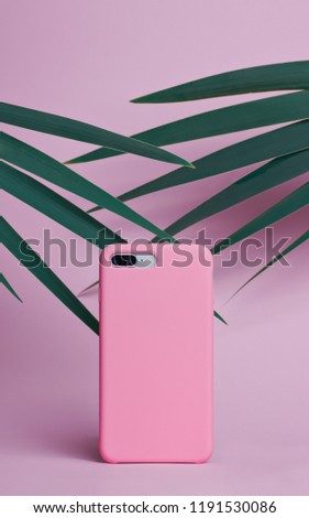 Smart phone on a pink background of palm leaves in a pink plastic case back view. Template of phone case