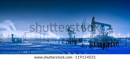 Oil and gas industry. Panoramic of a pump jack and oil refinery in the winter with snow. Night view.