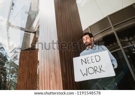 Low angle of serious executive standing at entrance of company. He is holding plaster displaying he needs work. Copy space in left side