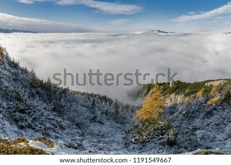 Aerial view on mountains and clouds. Autumn landscape with snow covered slopes