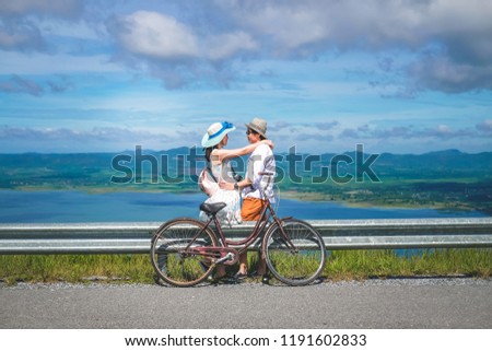 couple traveler standing beside bicycle background is mountain and dam on vacation.Asia tourists have romance time and enjoying for holiday.