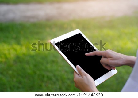 Hand holding smartphone or tablet on green nature background