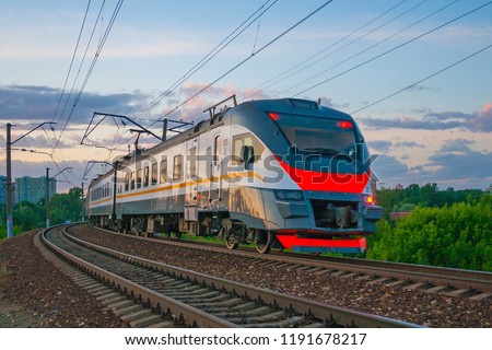 Passenger electric train moves against the background of green trees and evening sky Royalty-Free Stock Photo #1191678217