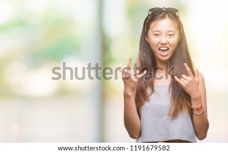 Young asian woman wearing sunglasses over isolated background shouting with crazy expression doing rock symbol with hands up. Music star. Heavy concept.
