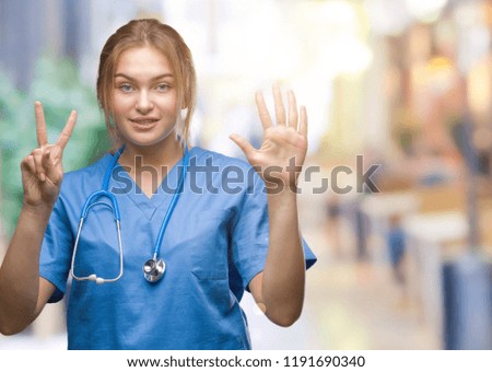 Young caucasian doctor woman wearing surgeon uniform over isolated background showing and pointing up with fingers number seven while smiling confident and happy.