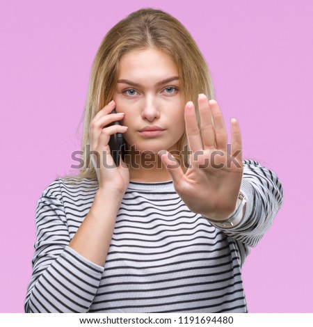 Young caucasian woman showing smartphone screen over isolated background with open hand doing stop sign with serious and confident expression, defense gesture
