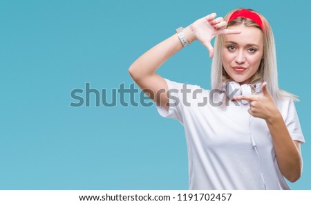 Young blonde woman wearing headphones listening to music over isolated background smiling making frame with hands and fingers with happy face. Creativity and photography concept.